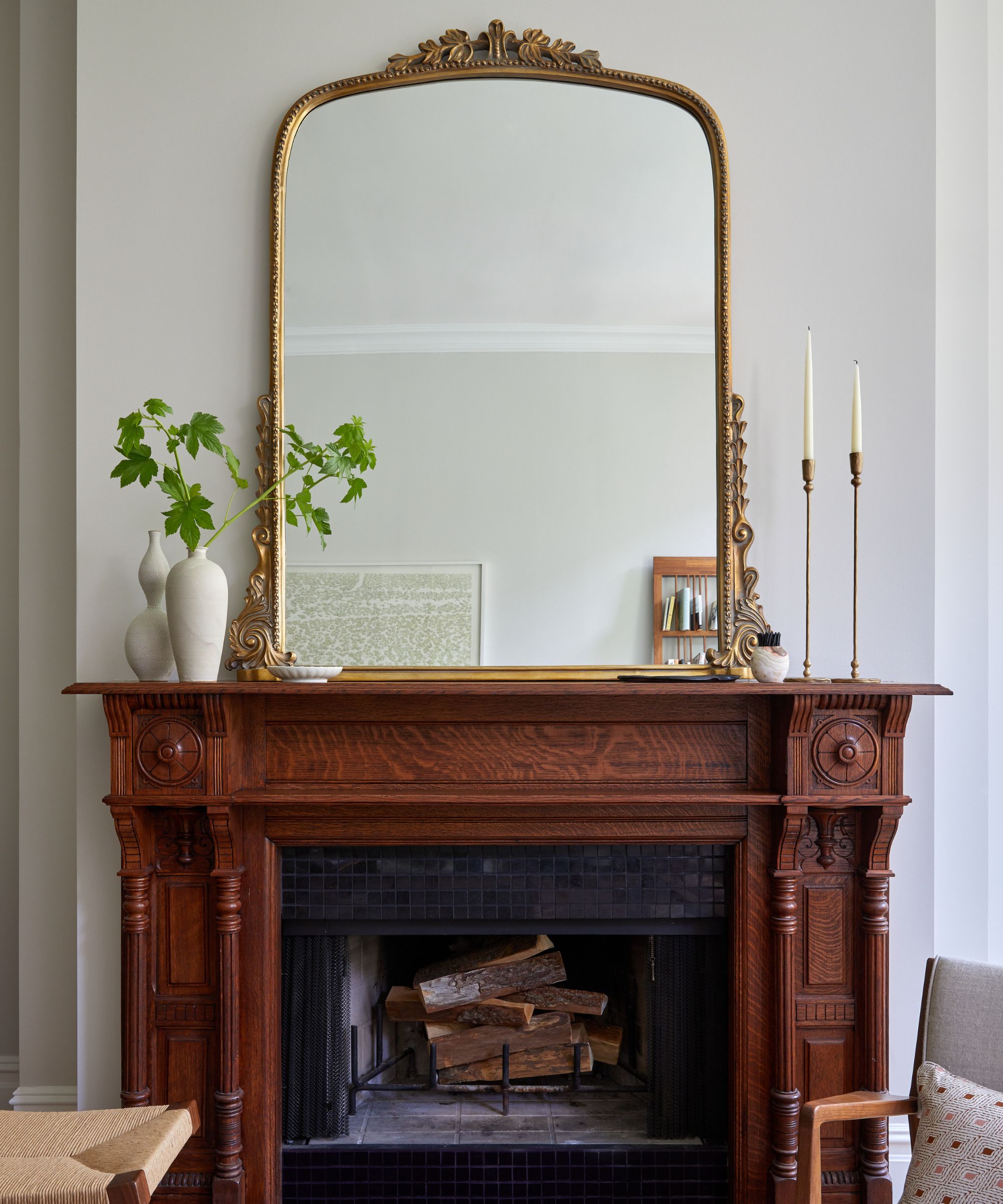 A living room with light gray walls and a wooden fireplace with a large vintage mirror above it.