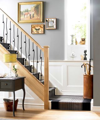 A staircase railing idea by Richard Burbridge with matte black balustrades and white oak stairs with umbrella holder and framed art