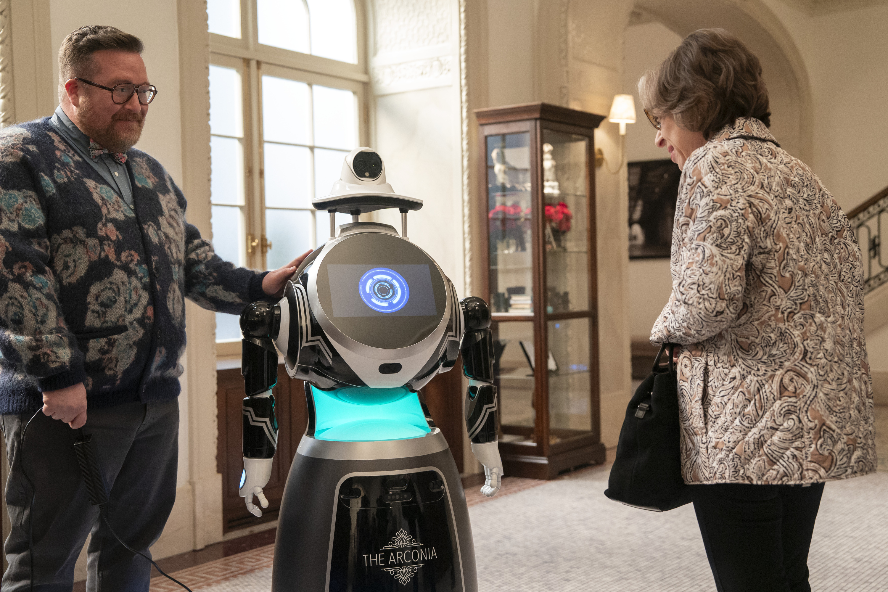 MICHAEL CYRIL CREIGHTON and JACKIE HOFFMAN talk to a robot in the lobby of the arconia in only murders in the buliding season 5