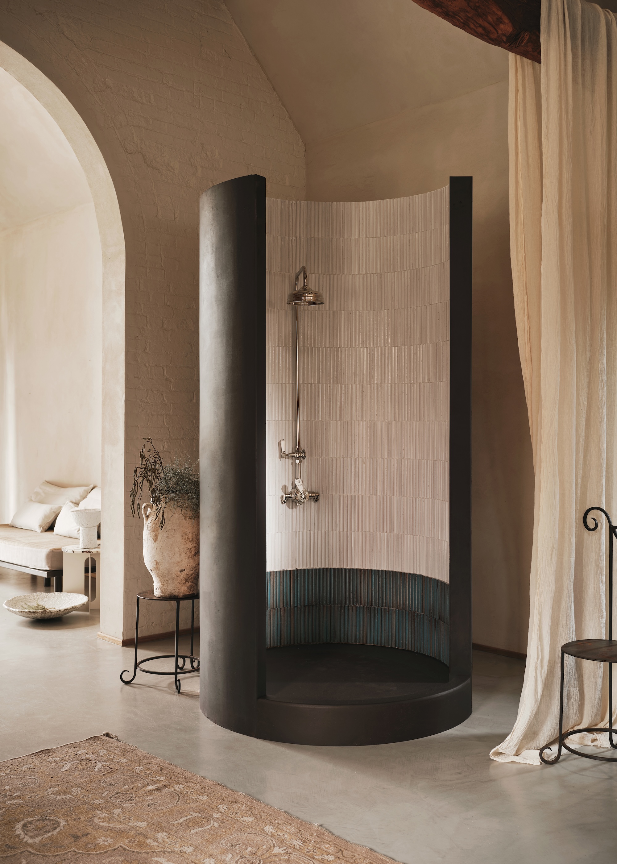 a curved black shower with cream tiling on the inside and an arched doorway leading to the rest of the bathroom