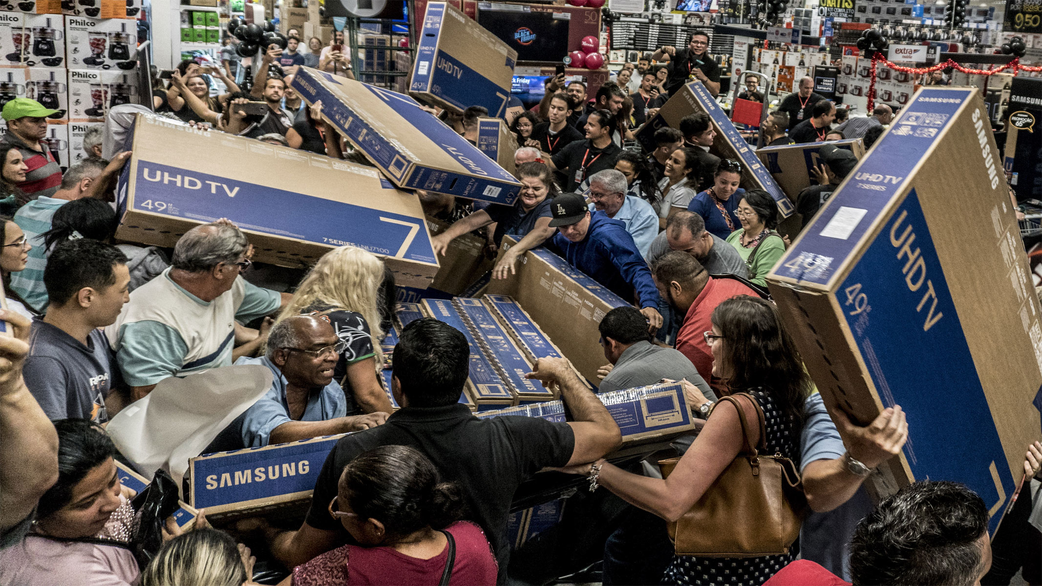 Image shows a large group of shoppers grabbing TVs inside a store during a Black Friday sale