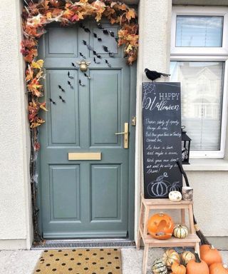 A halloween door decorating idea with teal door paint, chalkboard signage and assortment of carved and lit pumpkins
