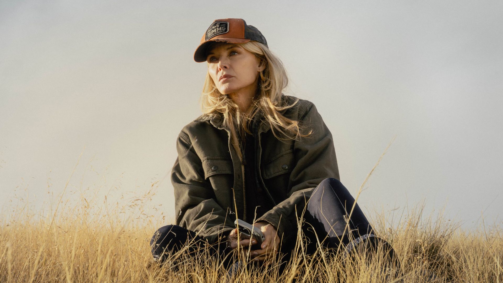 Michelle Pfeiffer sits on a grassy hill