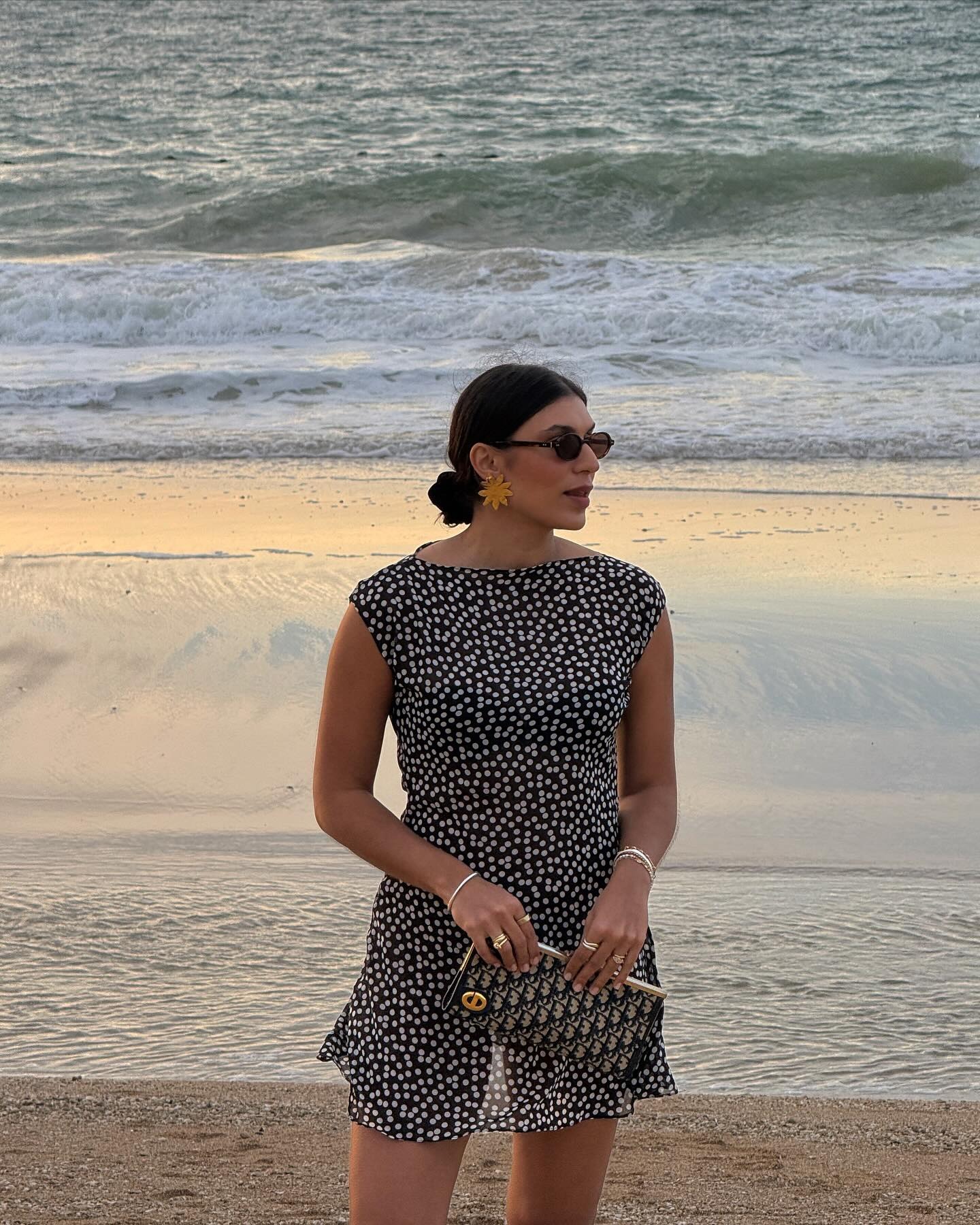 Fashion person India wears a sheer susamusa polka dot dress large gold flower earrings and is carrying a Dior clutch bag in an image taken from her Instagram recently.