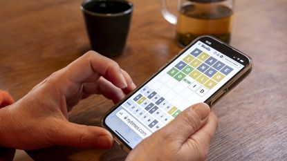 A person holding a phone showing a game of Wordle on the screen