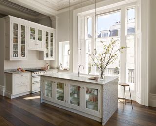 white kitchen with stone countertops, glass fronted cabinets, wooden floor