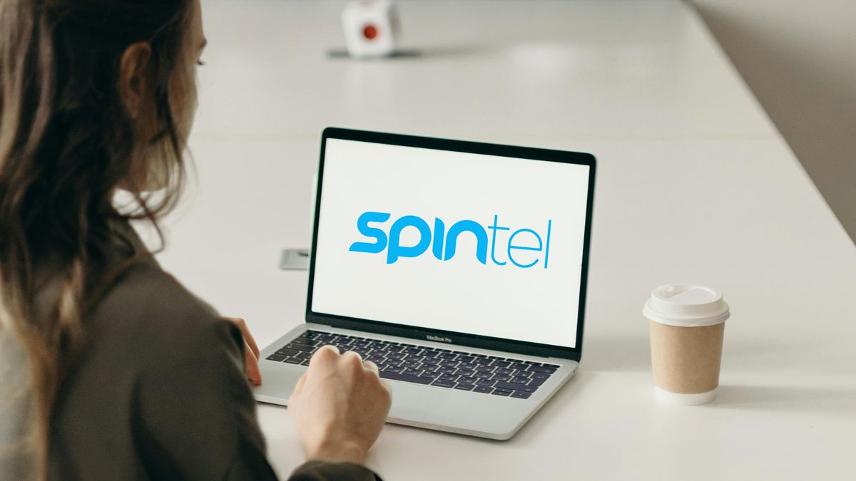 Woman at laptop looking at SpinTel Logo on screen with a coffee cup next to her