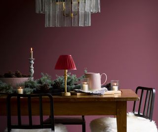 wooden dining table with dark pink wall and red lamp