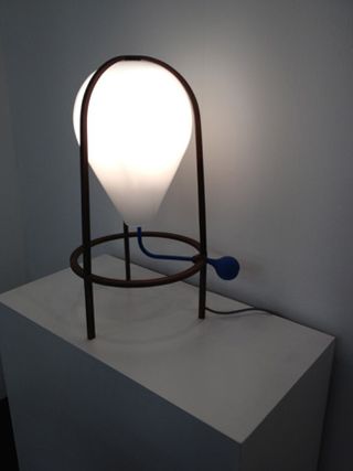 White wall, white block viewing platform, metal frame lamp, white ballon shape shade lit up, blue switch, black cord