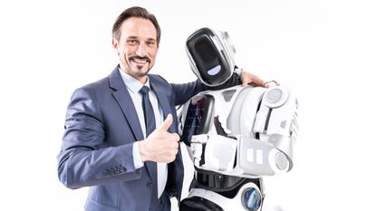 A man dressed in a suit embracing a cyborg, both of them facing the camera and holding a thumbs up
