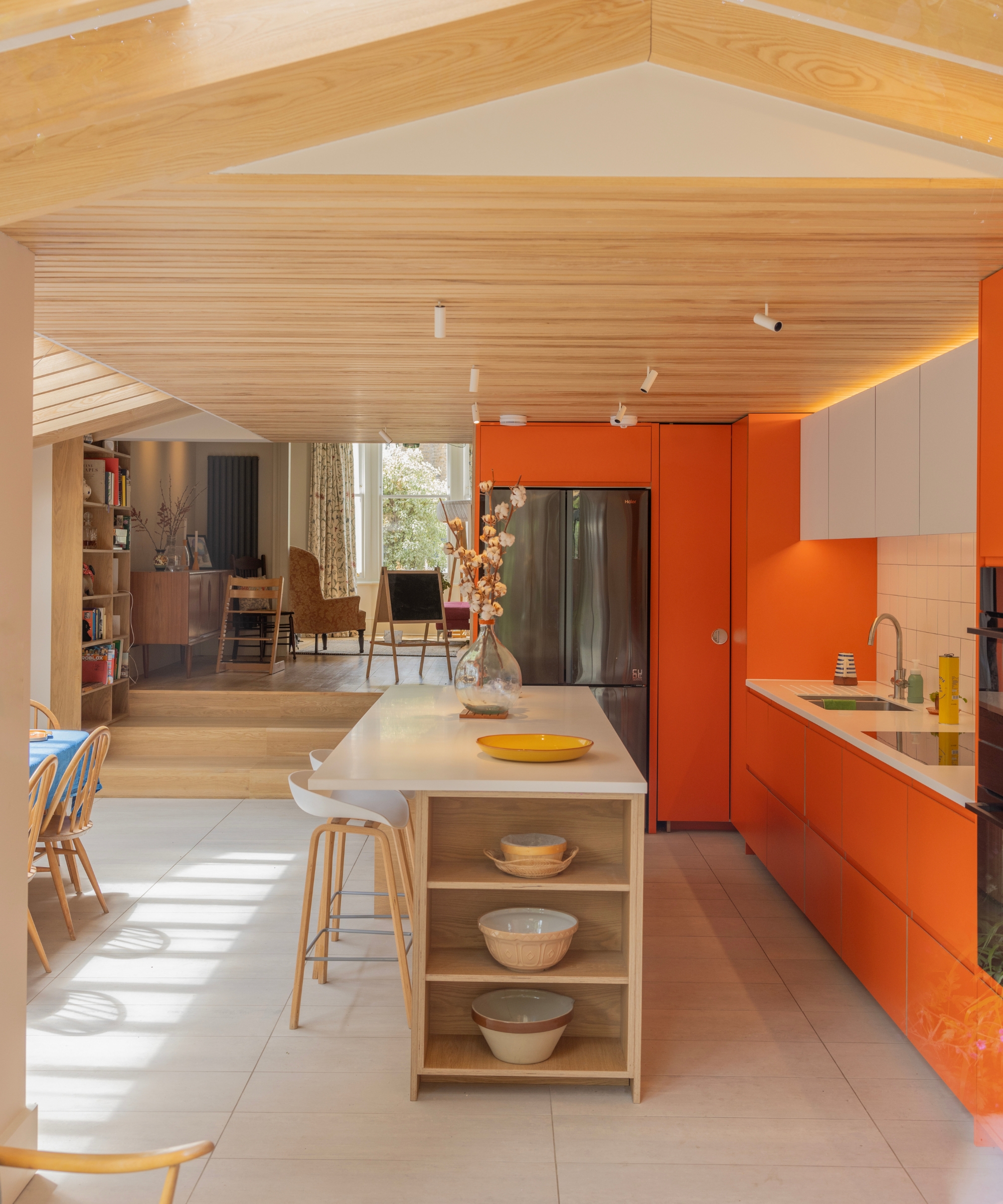 Kitchen with orange cabinetry and wooden vaulted ceiling, island with open shelving, view to living room.