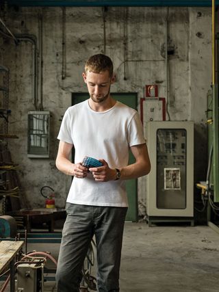 A young man with short hair wearing a white tee and jeans holding a glass vessel.