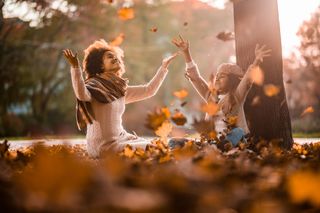 A woman and child play in fallen leaves