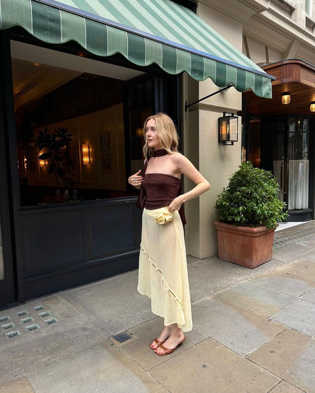 Influencer Chloe Butler wears a butter yellow sheer skirt, a brown tube top, and brown kitten heel sandals.