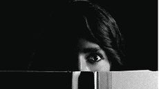 Black and white illustration of a woman's eyes over the top of a book, looking scared