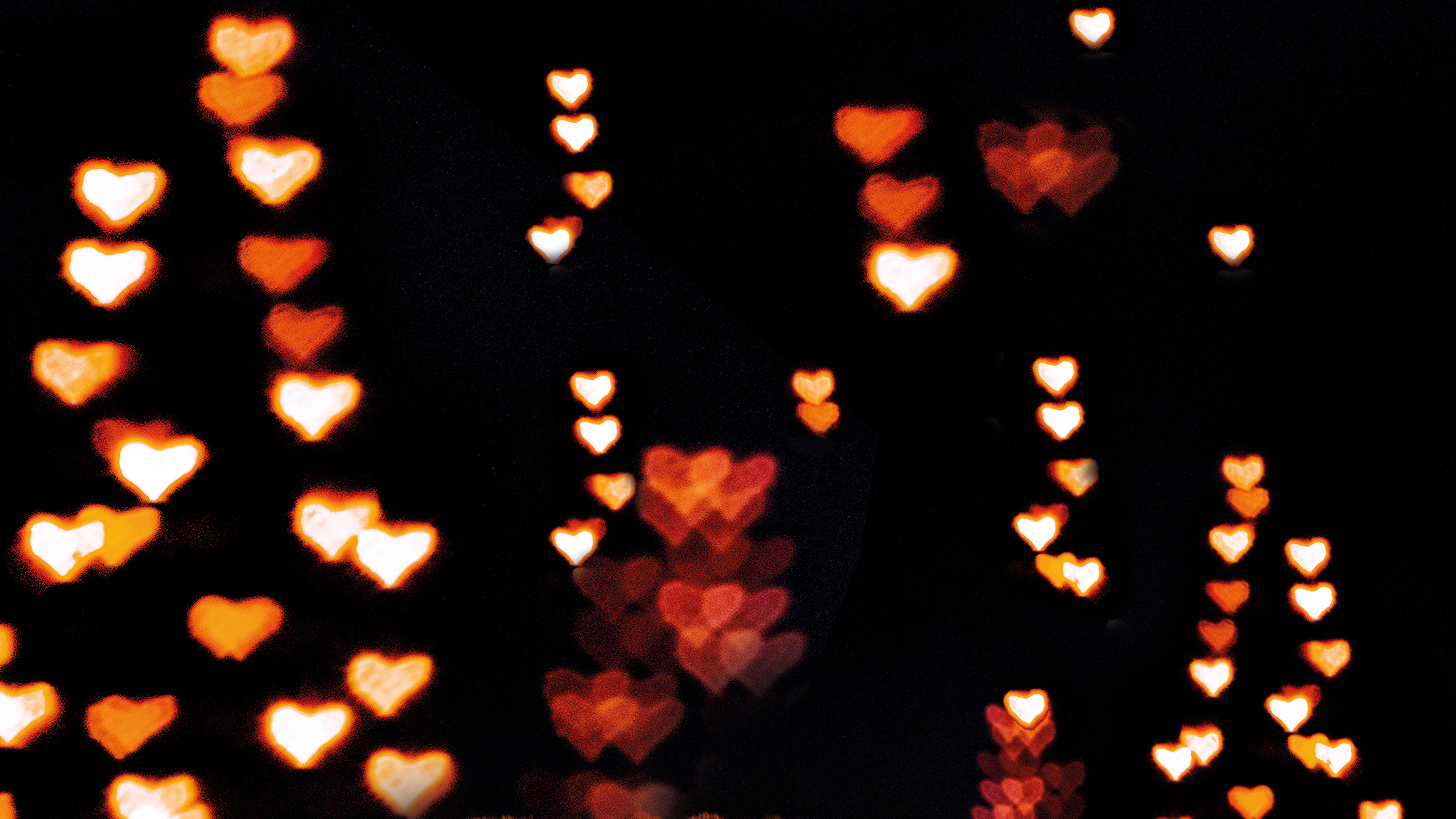 A blurred background filled with glowing heart-shaped bokeh lights in warm hues of orange, red, and white against a dark backdrop