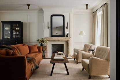 A cream living room with a wooden coffee table, orange accent sofa and neutral palette. 