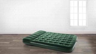 Image shows a deep green blow up mattress on a wooden floor in a white room