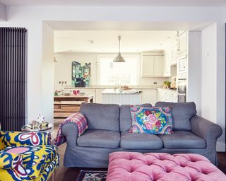 An open plan living room with statement yellow armchair and pink footstool with white kitchen in background