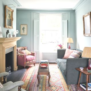 blue living room with pink chair and grey sofa opposite a wooden fireplace