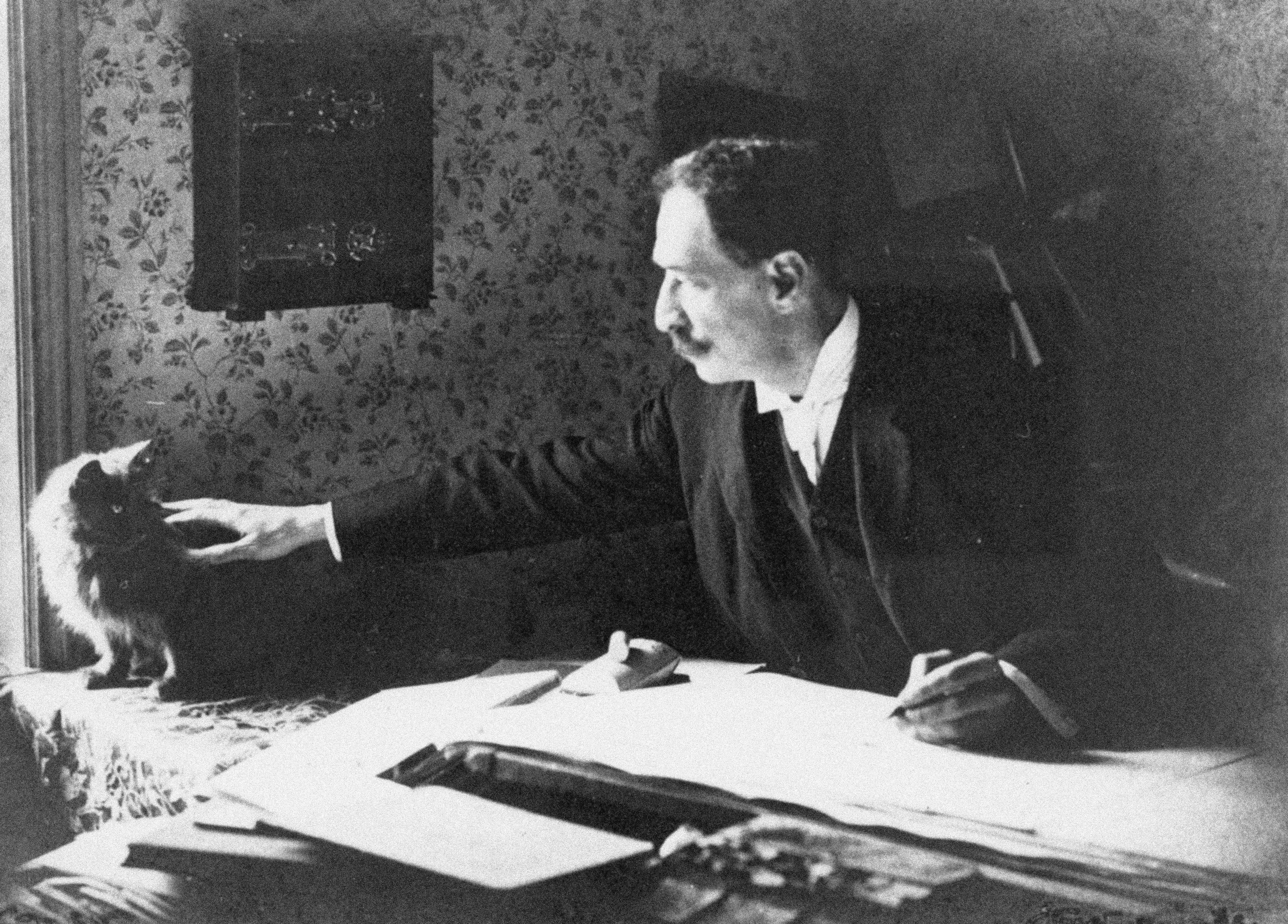Louis Wain at his drawing board in the 1890s with a cat.