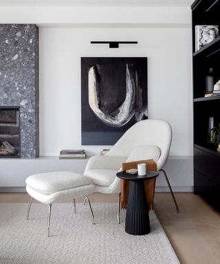 living room with a white boucle mid century modern style chair and foot rest with a large piece of black artwork on the wall behind