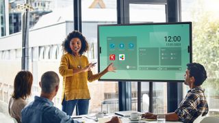A female presenter shows her screen on a display in an all-window conference room. 