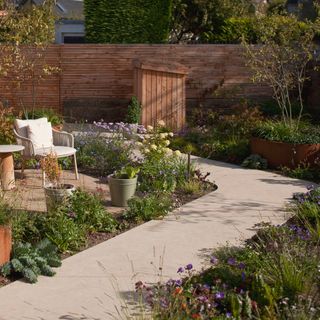 a garden with a winding pathway to a fence door, with a mini shed, and seated area