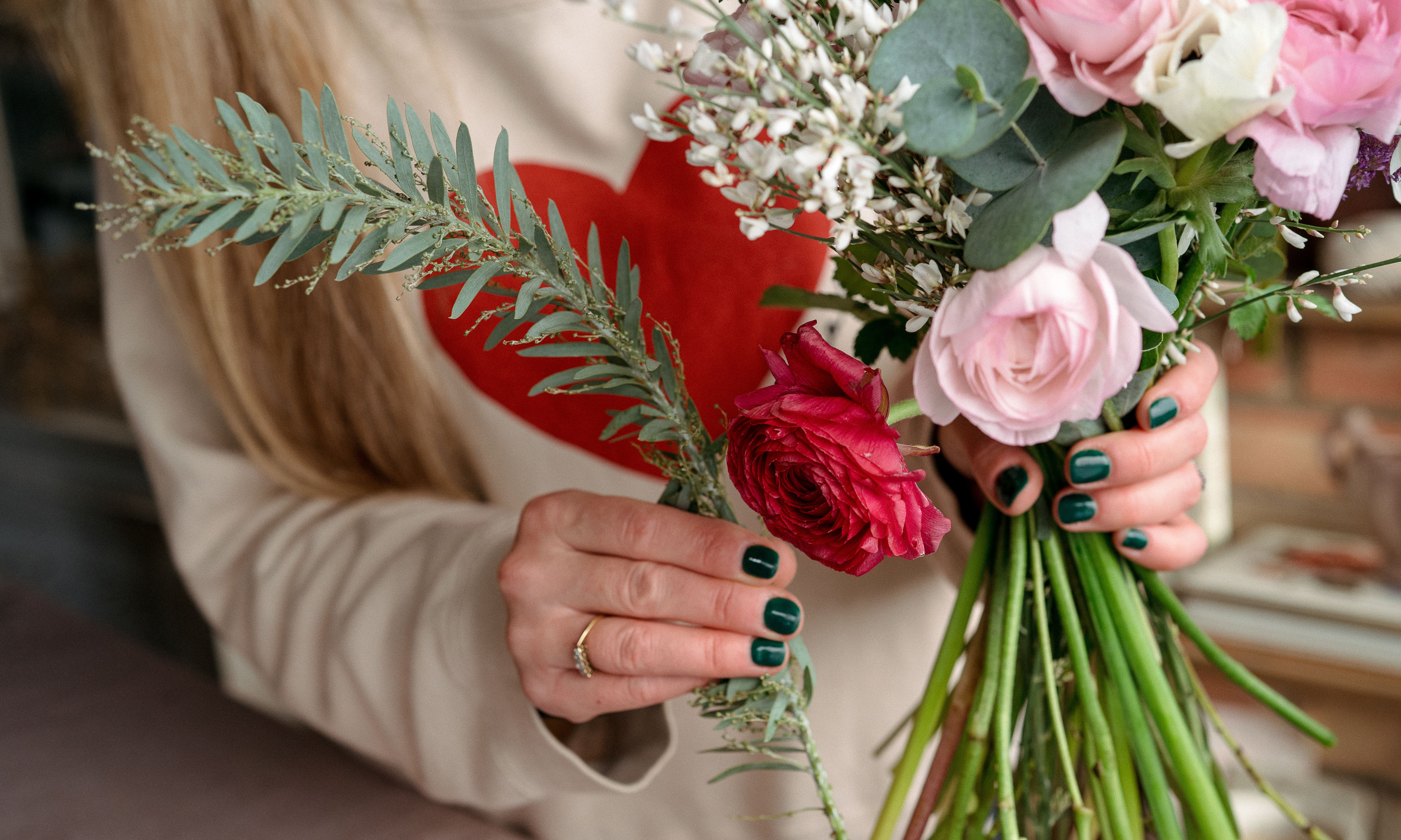 Hand placing a stem of mimosa foliage into a handtied bouquet