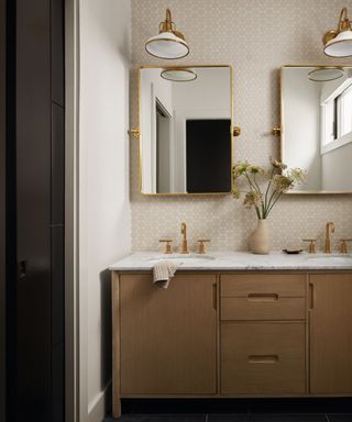 A bathroom with wooden cabinets, two gold mirrors and tiled walls