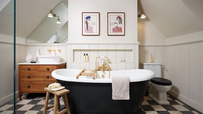 freestanding bath on white and black tiles in front of white paneled wall with artwork