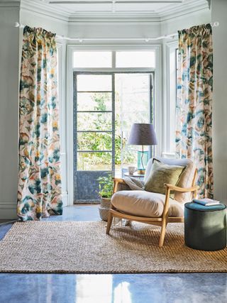 Mid century upholstered armchair on rug by French door to garden, curtains with floral pattern