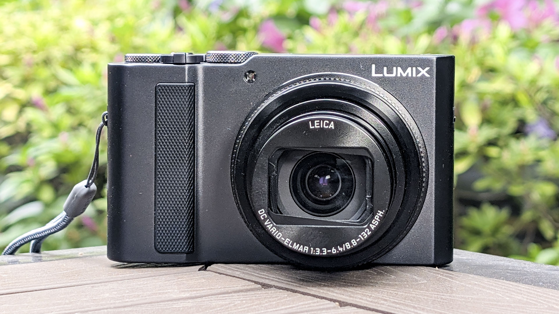 Panasonic Lumix TZ300 compact camera on a wooden table, with a colorful floral backdrop