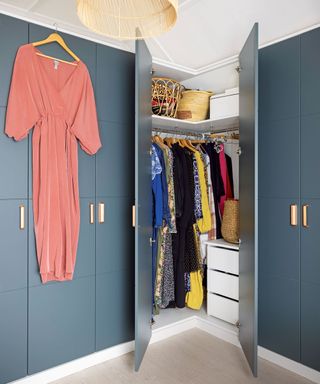 Fitted wardrobes painted blue with hanging clothes inside and pink jumpsuit hung on hanger on door