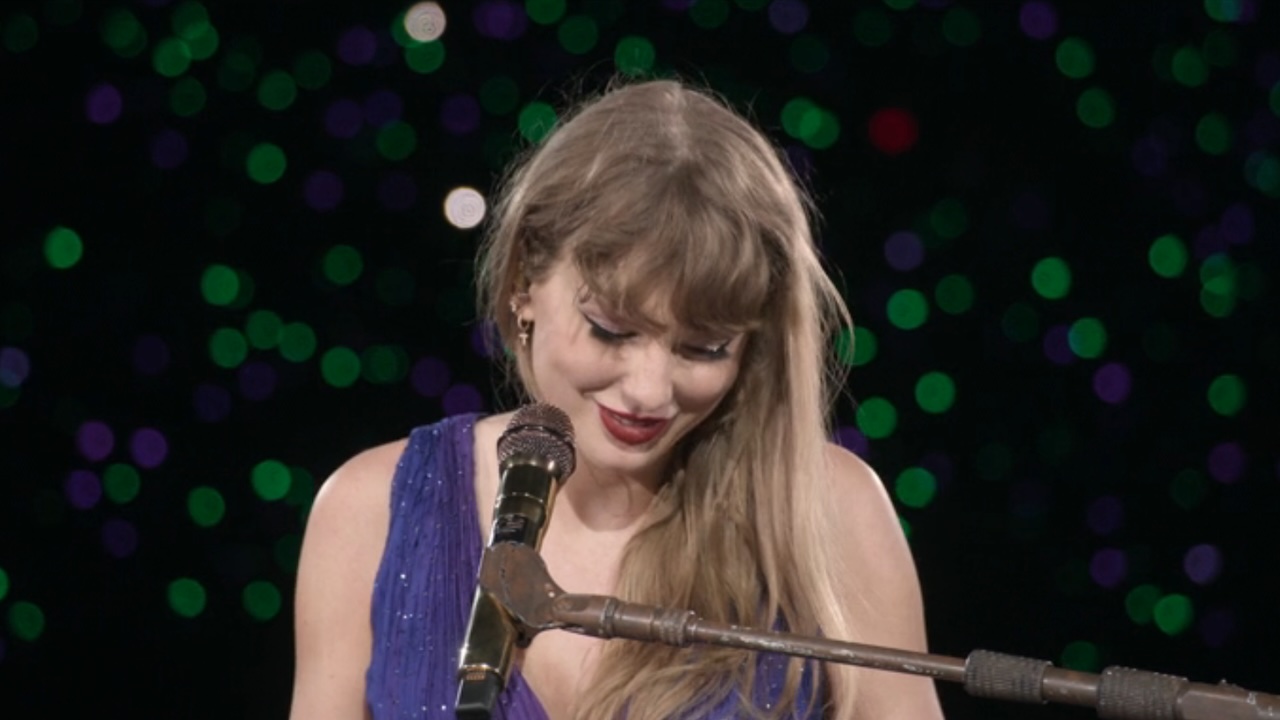 Taylor Swift smiling behind a microphone at The Eras Tour