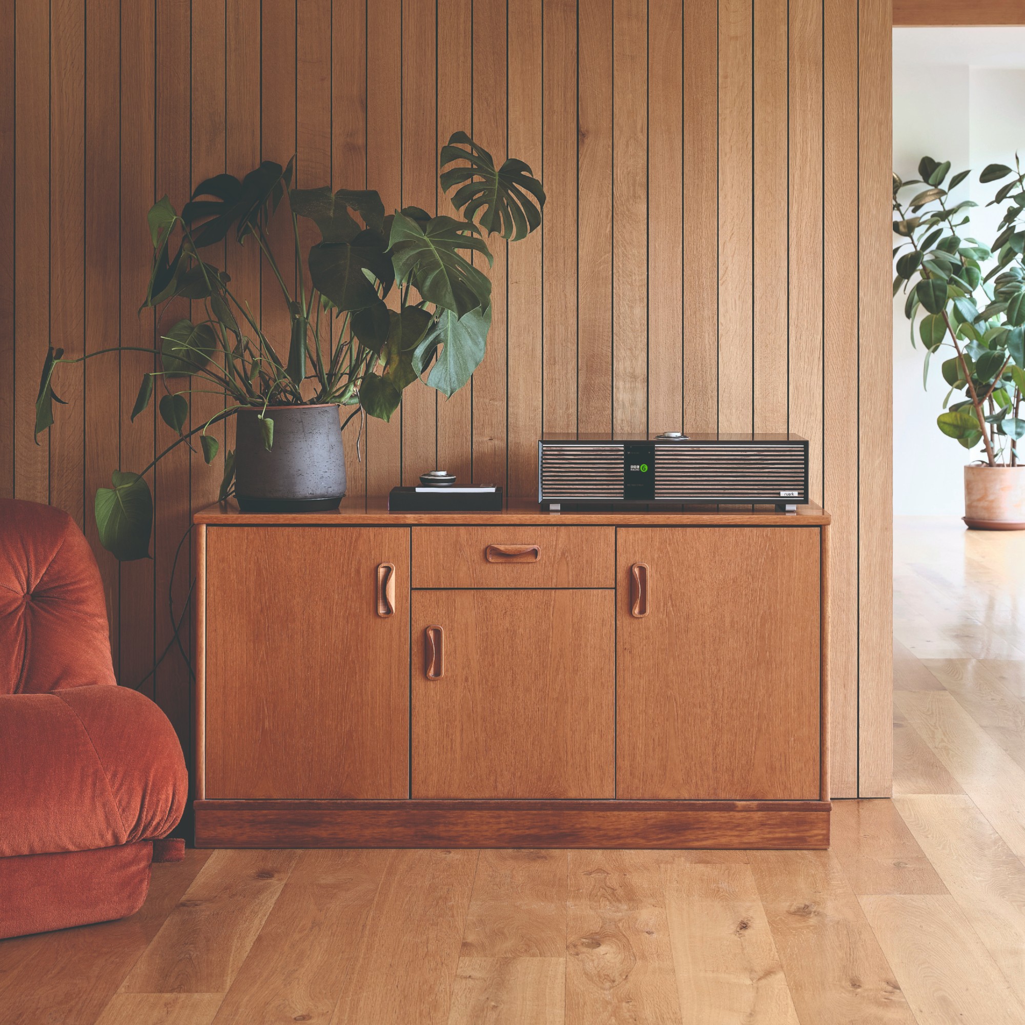 The R410 All-In-One Music System by Ruark Audio displayed oon a midcentury cabinet with a large plant against a panelled wall
