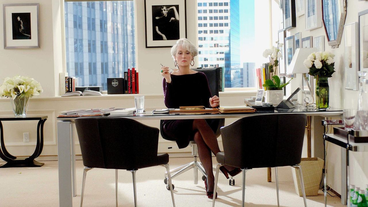 White office with black chairs, transparent desk and silver framed artwork on walls 