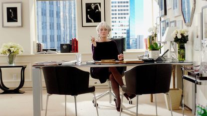 White office with black chairs, transparent desk and silver framed artwork on walls 