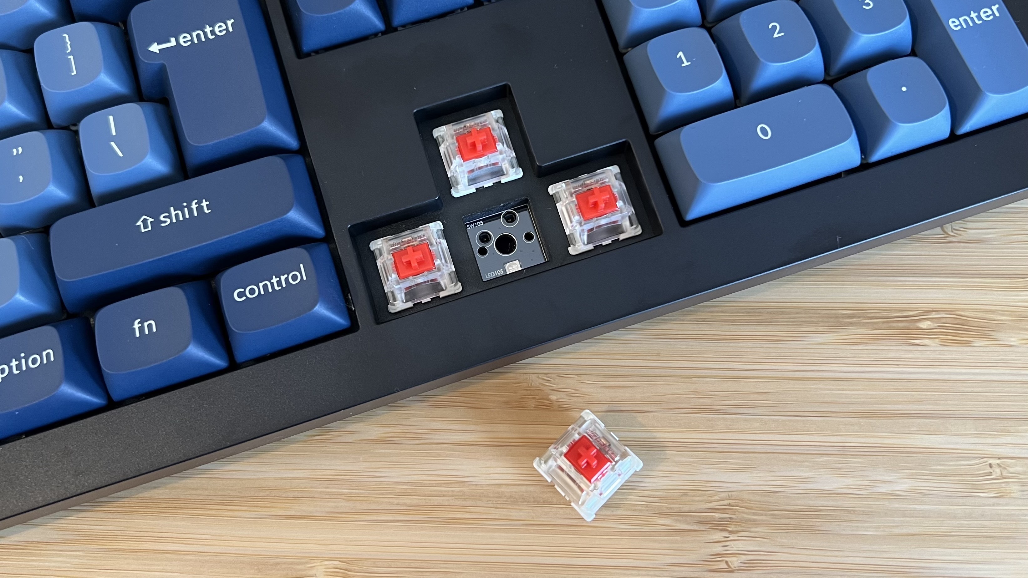 Close up on red linear switches inside Keychron V6 Max keyboard, with one removed to show PCB underneath
