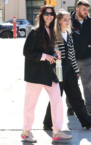 Anne Hathaway wearing a black blazer, pink sweatsuit, and pink Nike sneakers in NYC