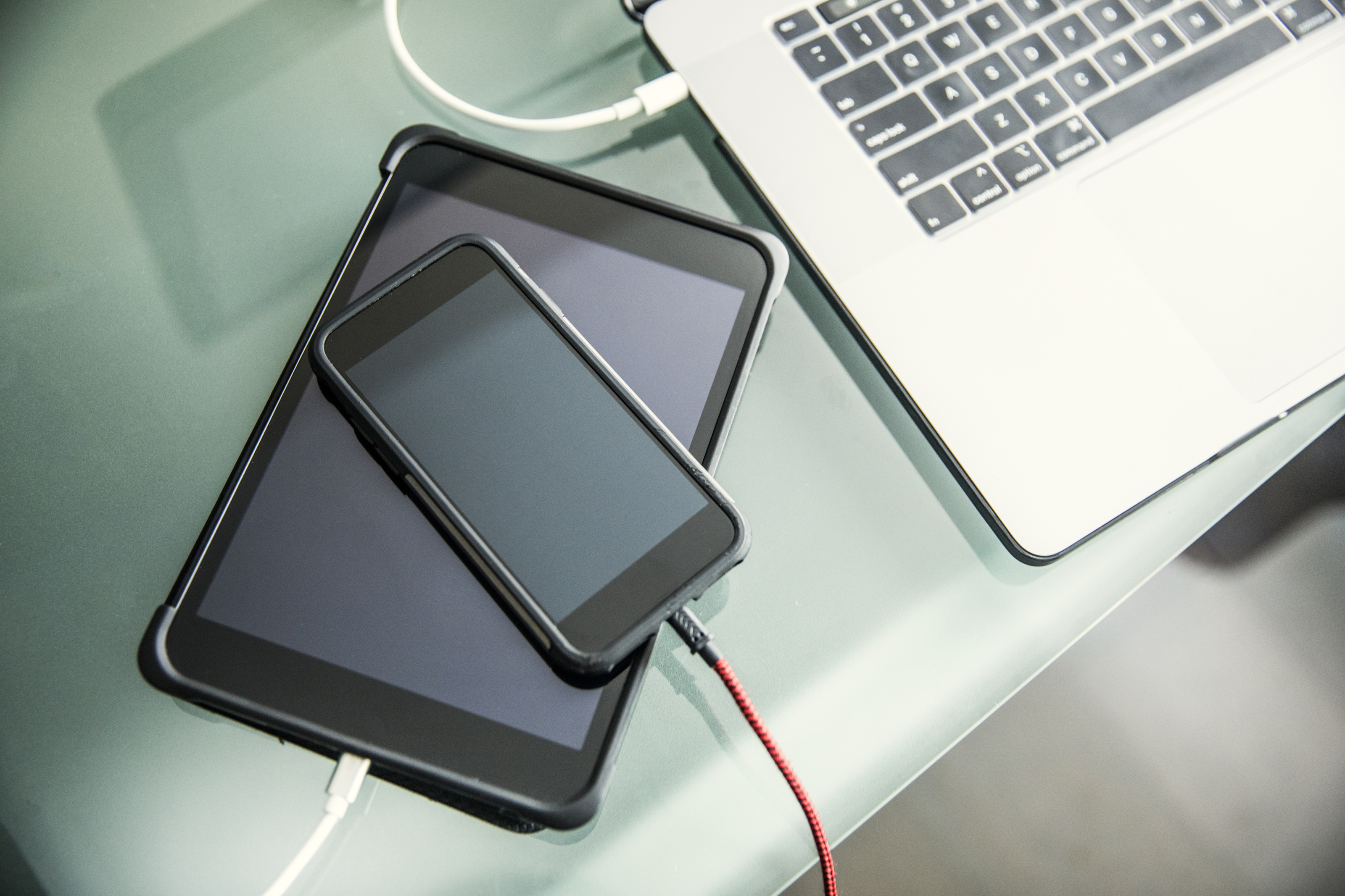 An iphone, ipad, and laptop all charging on a table