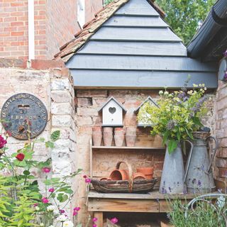 Potting bench with terracotta pots and metal jugs against brick wall with wall art