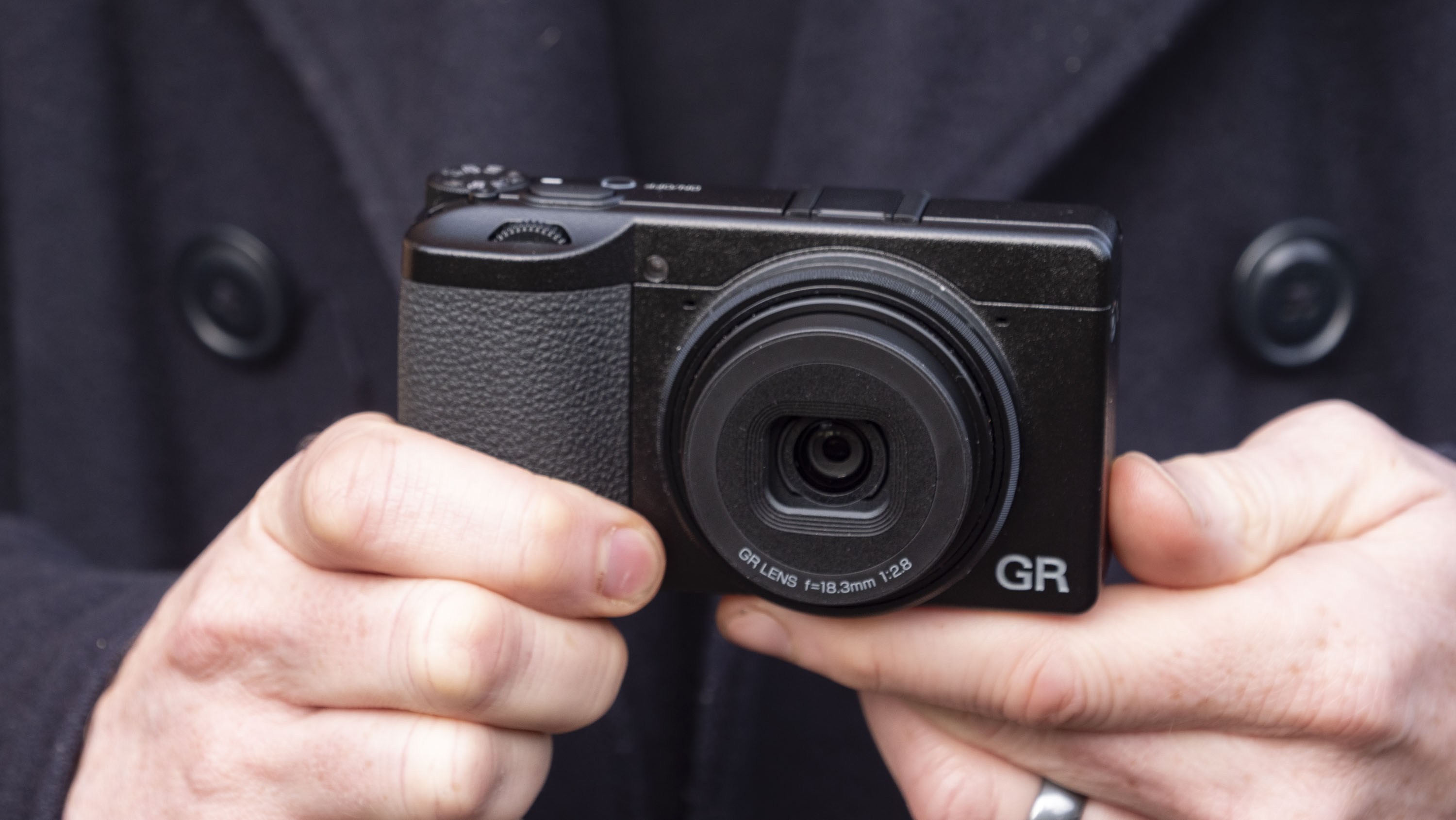 Ricoh GR IV compact camera in user's hand, they are wearing a winter jacket