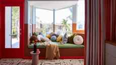 Image of a green bench seat with colorful round pillows in a bay window. The walls are a white and dark orange color block, and the doors and trim are painted bright red.