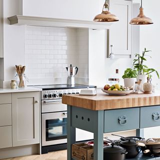 white kitchen with green wooden topped island and metallic pendant lights