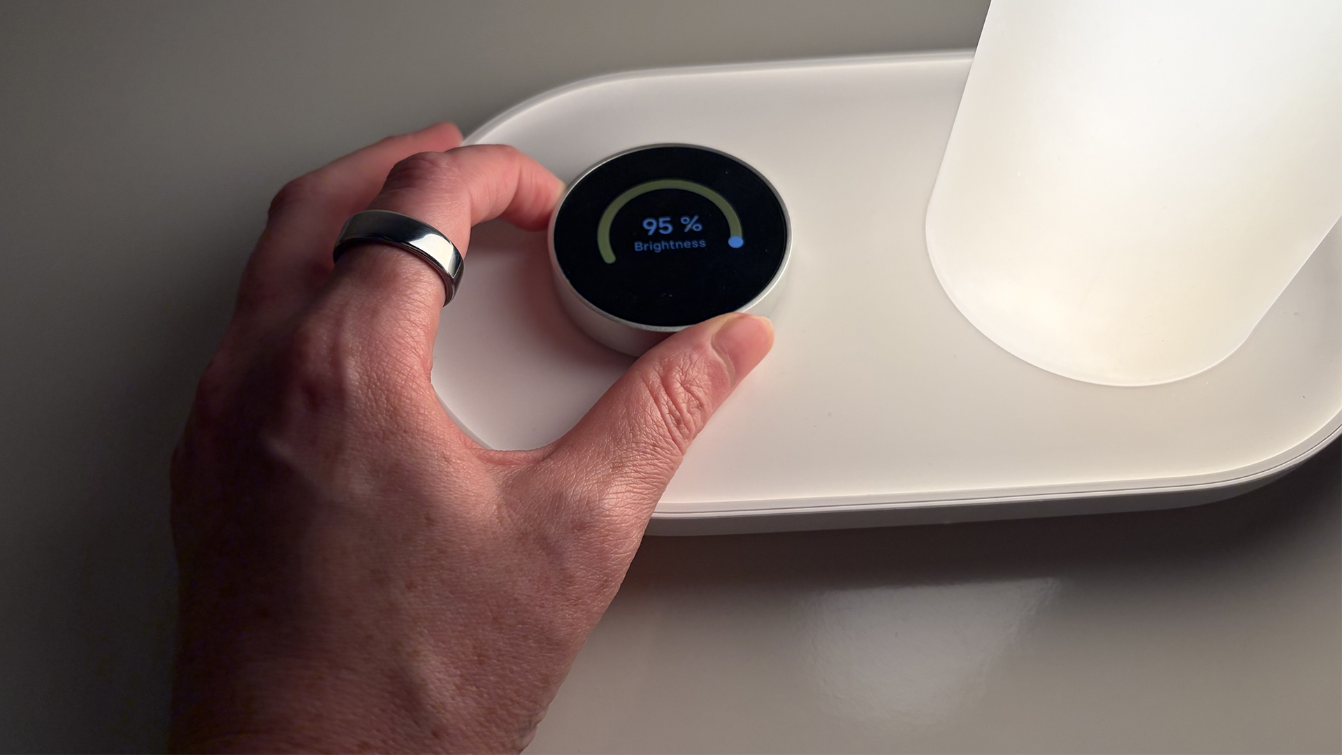 A close up of a hand adjusting the brightness of the Sleepal AI Lamp using the control button on the base of the lamp