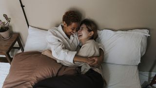 A couple lie on a bed smiling and cuddling each other