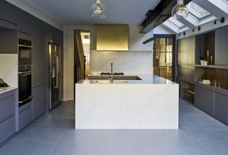 grey kitchen with white marble island in the middle, grey floor, gold cooker hood