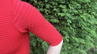 Shoulder view of man wearing red short-sleeved base layer by hedge