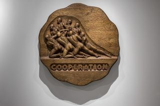 circular art piece with carved people and the letters cooperation